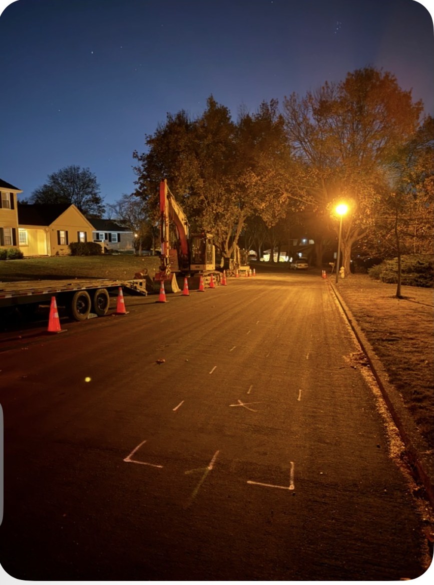 Excavator staged at a marked road opening on a residential street at night in Allentown, PA